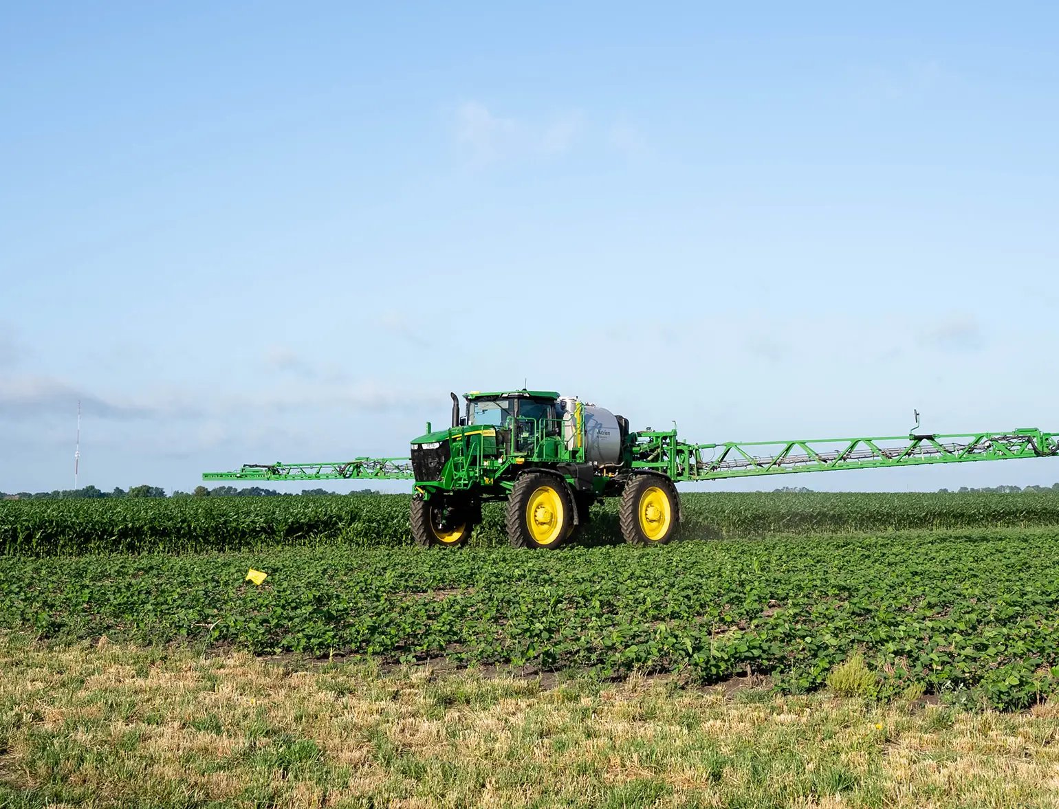 Field sprayer operating across a crop field under a clear blue sky.
